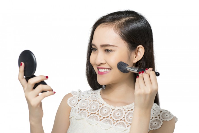 Young woman looking at the compact mirror and applying blush