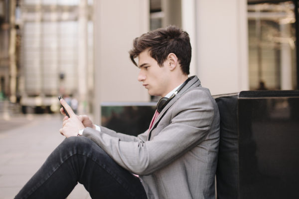 Young city businessman sitting on sidewalk reading smartphone messages