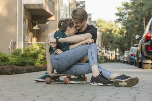 Happy young couple embracing while sitting on skateboard outdoors