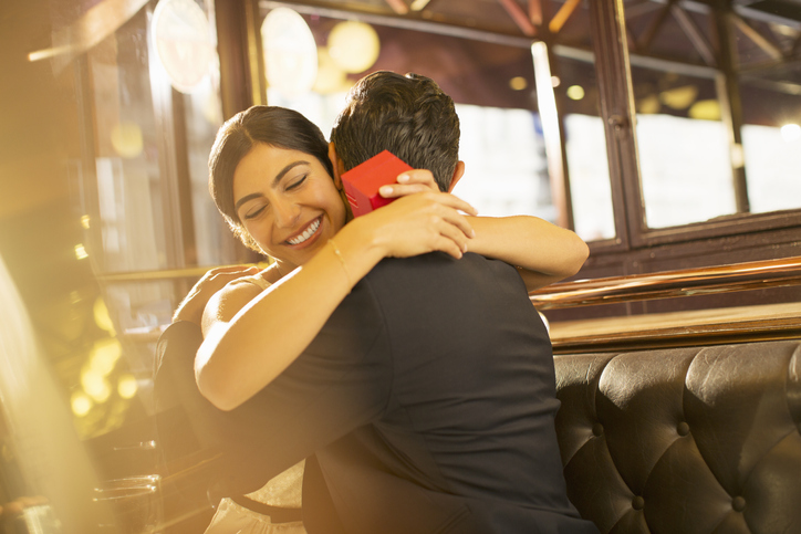 Woman with jewelry box hugging man in restaurant