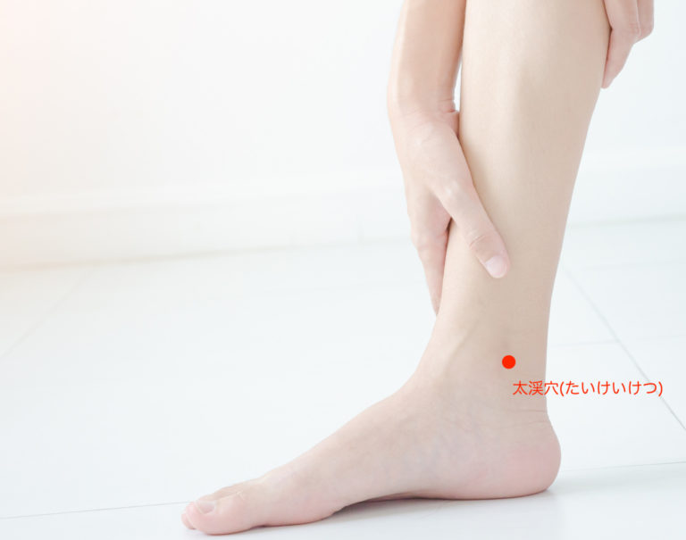 Asian girl wearing white dress have leg pain. The woman was squeezing her leg in a white bedroom with sunshine.Warm tone.Do not focus on objects.