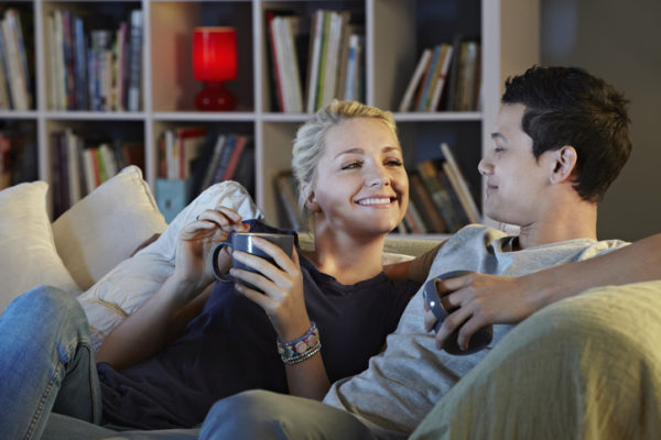 Young couple sitting on sofa with hot drinks