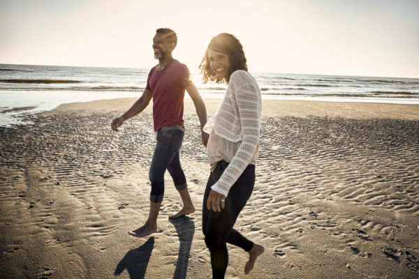 Happy mature man and young woman strolling on the beach at sunset