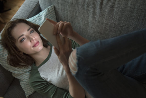 Caucasian woman laying on sofa texting on cell phone