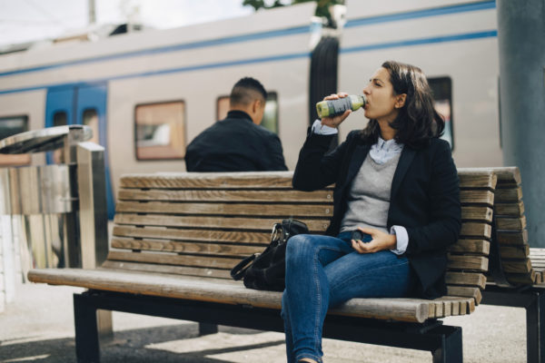 Woman drinking juice while sitting on bench at platform by train