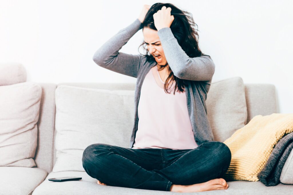 Frustrated Woman With Hand In Hair Sitting On Sofa At Home