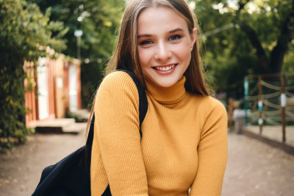 Portrait of pretty smiling student girl happily looking in camera in city park