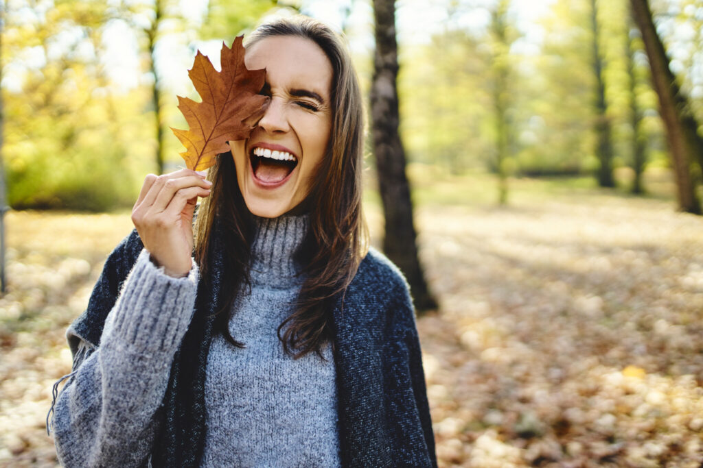 Young laughing woman holding autumn leave on her eye