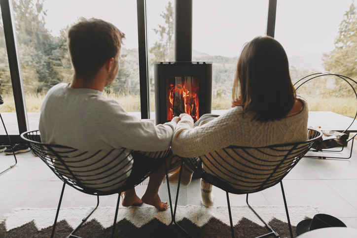 Stylish couple in sweaters relaxing together at modern black fireplace with view on mountains