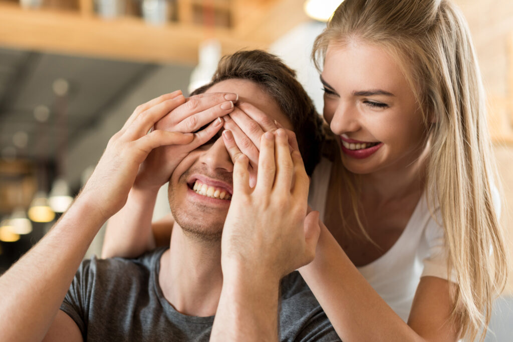 portrait of smiling woman covering boyfriends eyes with hands