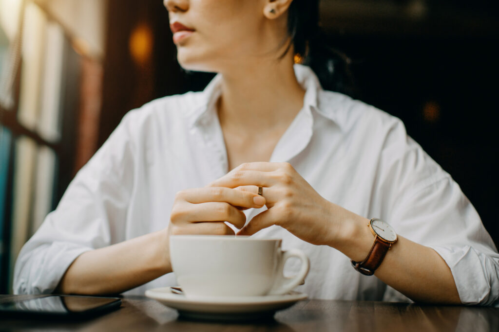 Woman touching the wedding ring on her finger nervously while having coffee and waiting in cafe