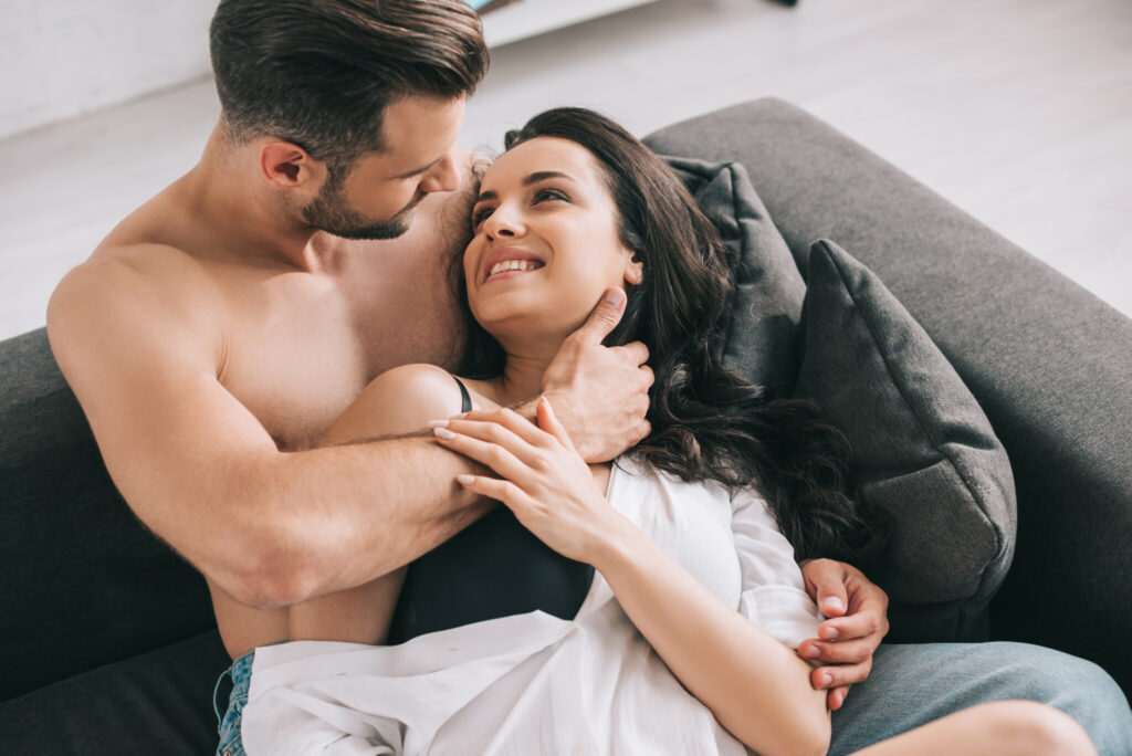 handsome man and sexy woman in shirt lying on sofa and hugging