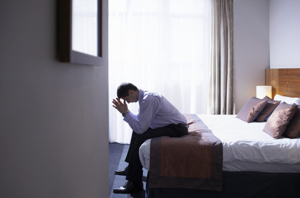 Man sitting on edge of bed with head in hands