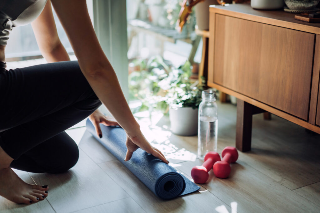 Close up of young Asian sports woman practicing yoga / exercising at home. Unrolling yoga mat, getting prepare to work out in the fresh bright morning