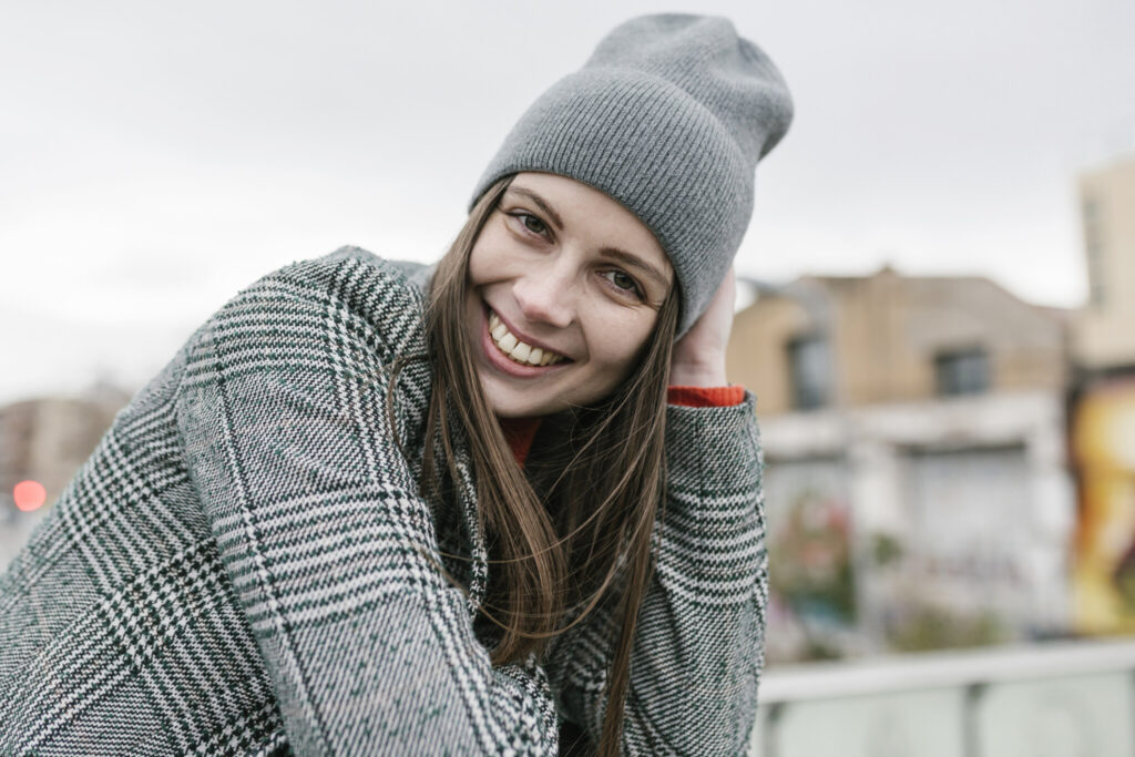 Smiling young woman in warm clothing with head in hand in city