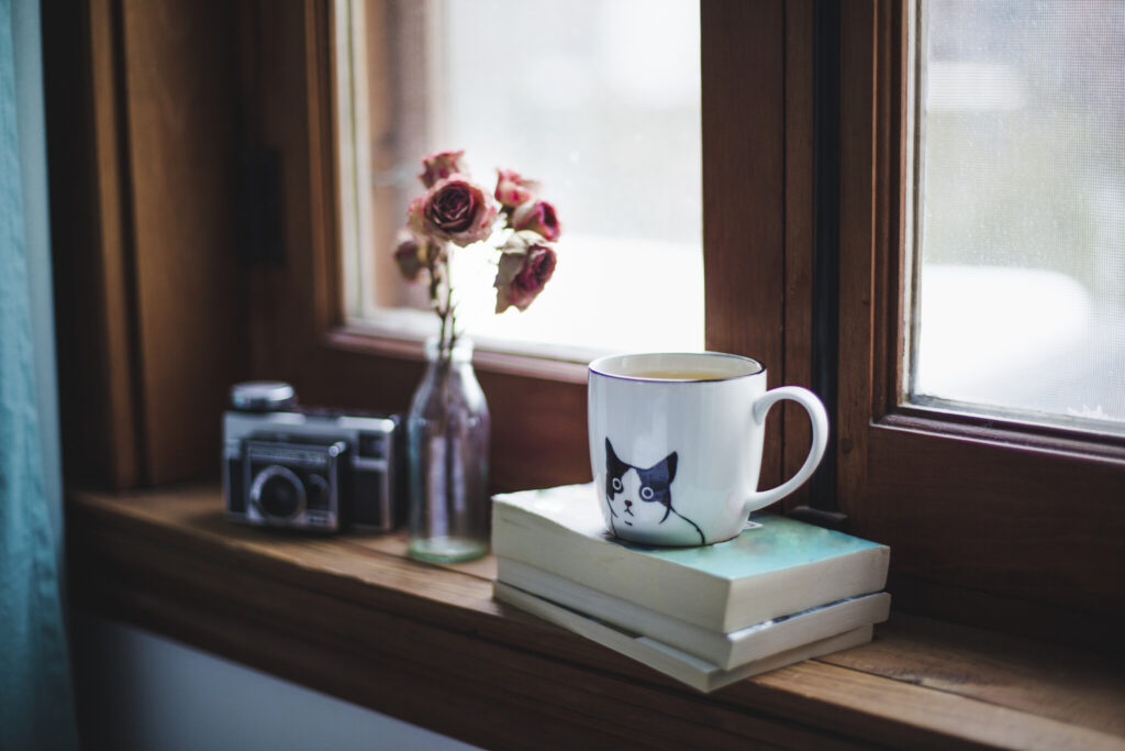 A cup of tea on books with dried roses on a window sill