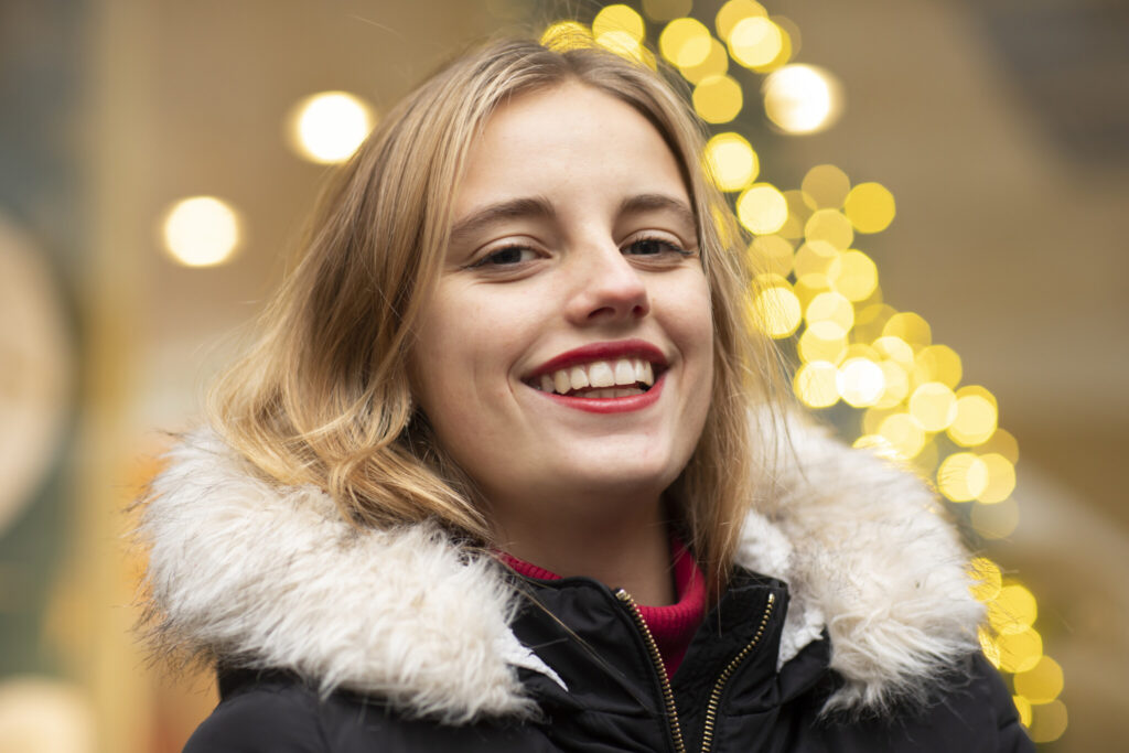 Bond young woman smiling against Christmas lights during holidays