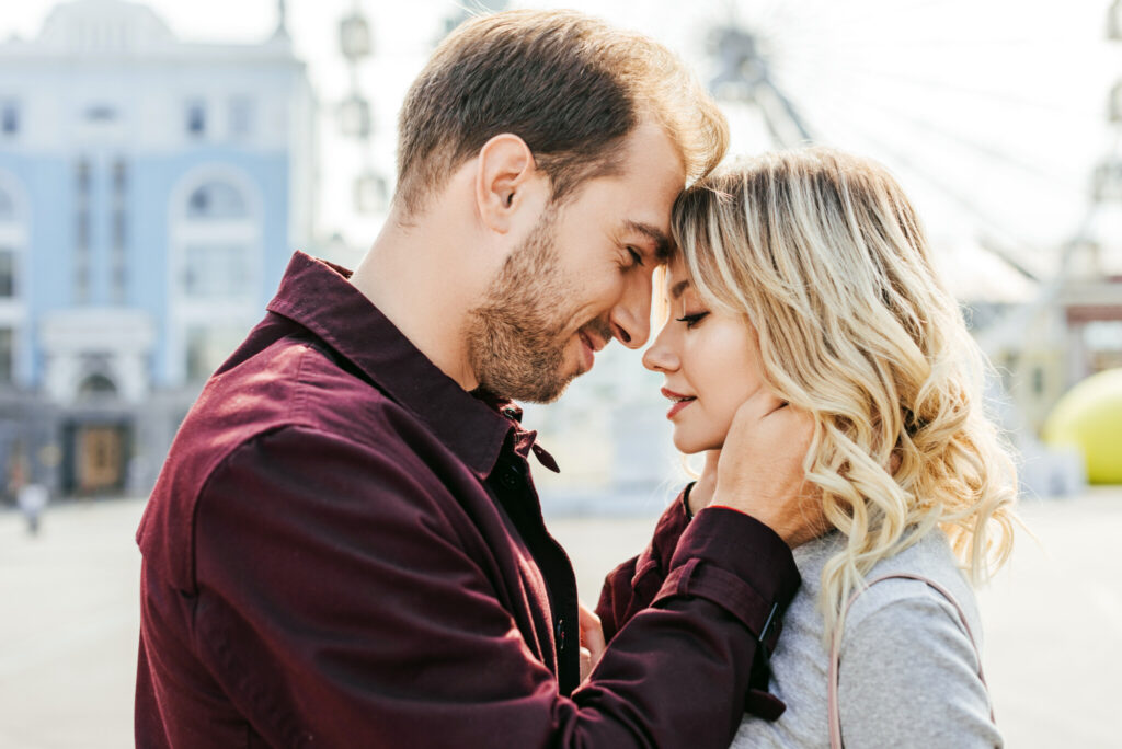side view of couple in autumn outfit touching with foreheads in city