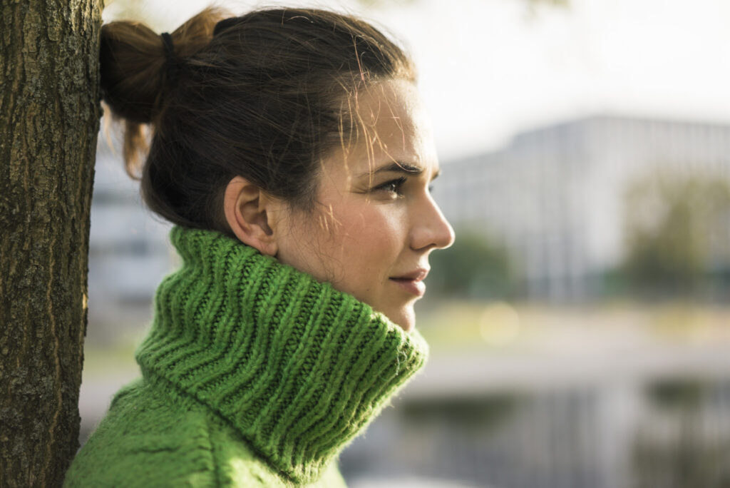 Profile of relaxed woman wearing green turtleneck pullover leaning against tree trunk