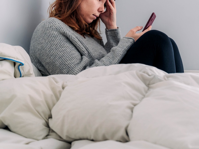Side View Of Woman Using Smart Phone While Sitting On Bed
