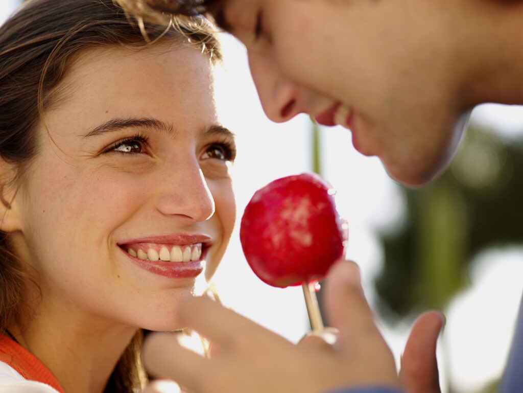Teenage couple (16-20) sharing candied apple on stick, close-up