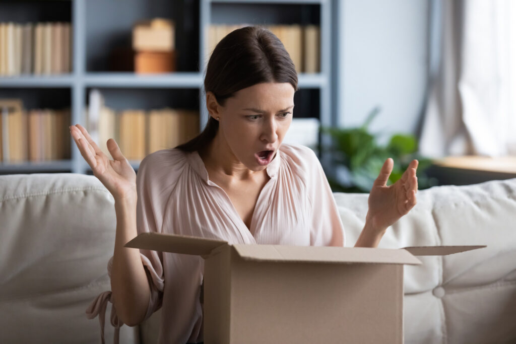 Angry shocked young woman unpacking parcel at home