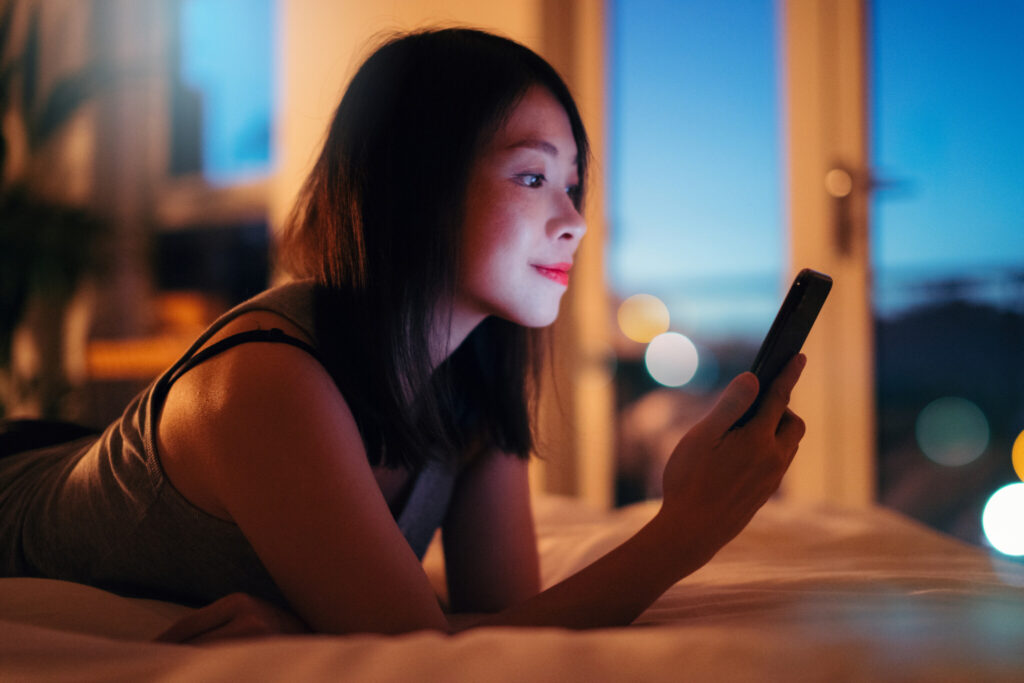 Young Woman Using Smartphone, Illuminated City Skyline In Background