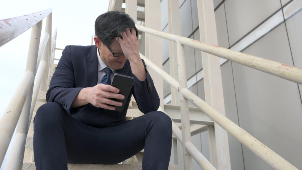 Depressed Asian adult businessman holding smartphone