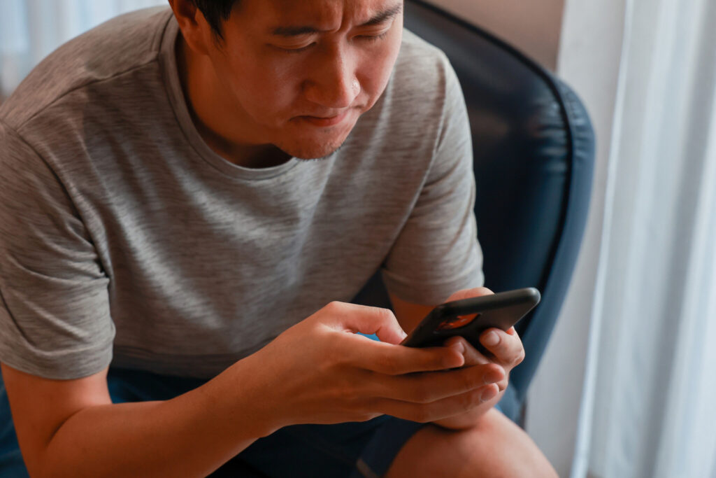 Yong Asian man using a mobile phone with frowning and worrying face expression with copy space