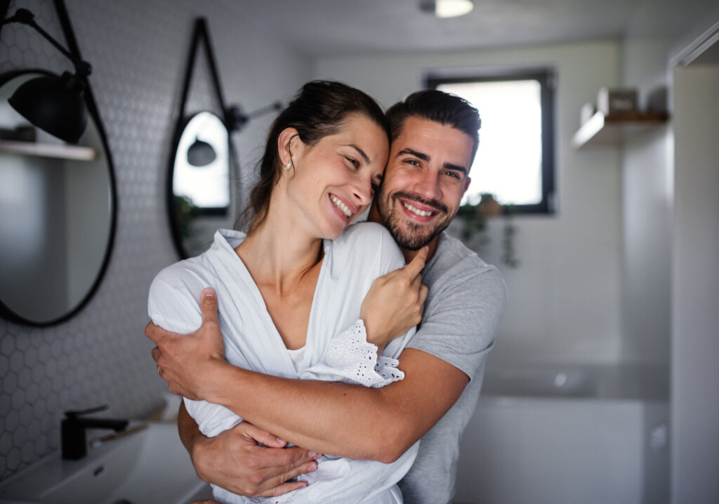 Portrait of young affectionate couple standing indoors in bathroom at home.