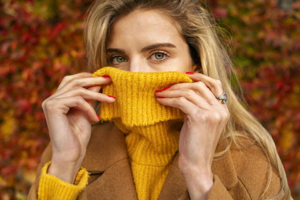 Closeup shot of beautiful blonde natural girl holding turtleneck sweater over her mouth, artistic portrait