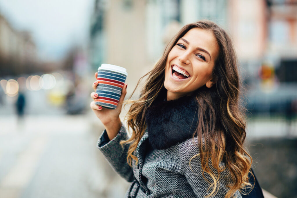 Young woman with coffee cup smiling outdoors