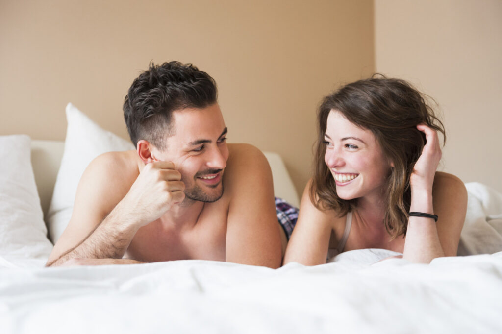 Happy young couple looking at each other while lying in bed at home
