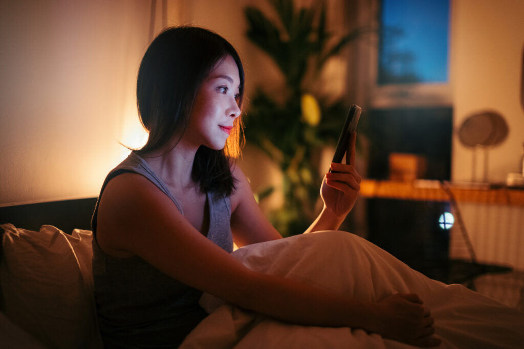 Young Woman Using Smart Phone Before Bedtime