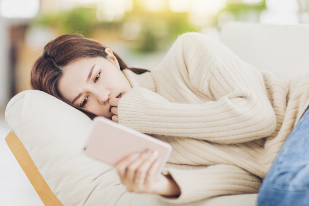 Stressed young woman lying on sofa watching the cellphone