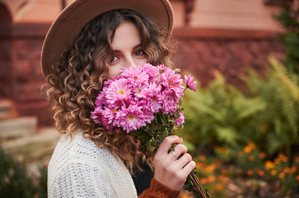Portrait of curly girl with bouquet of flowers near face.
