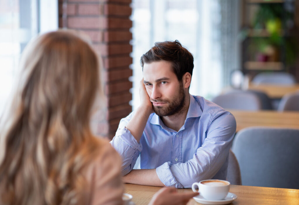 Young guy feeling bored on dull date at restaurant, disappointed in his partner