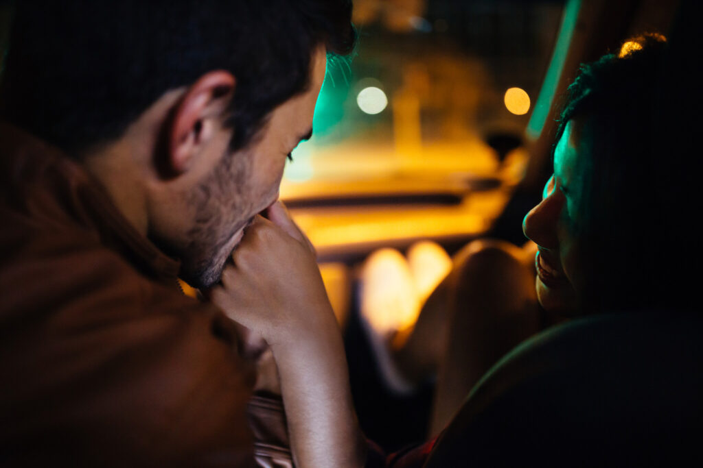Guy kissing his girlfriend’s hand in a car at night