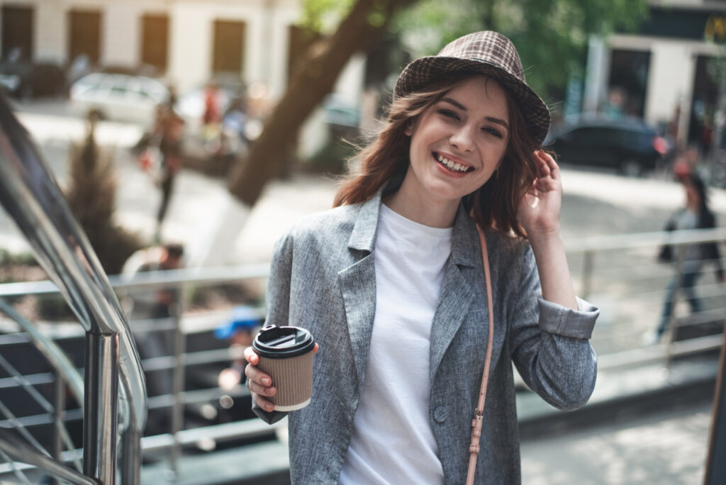 Young smiling lady standing outside with hot drink