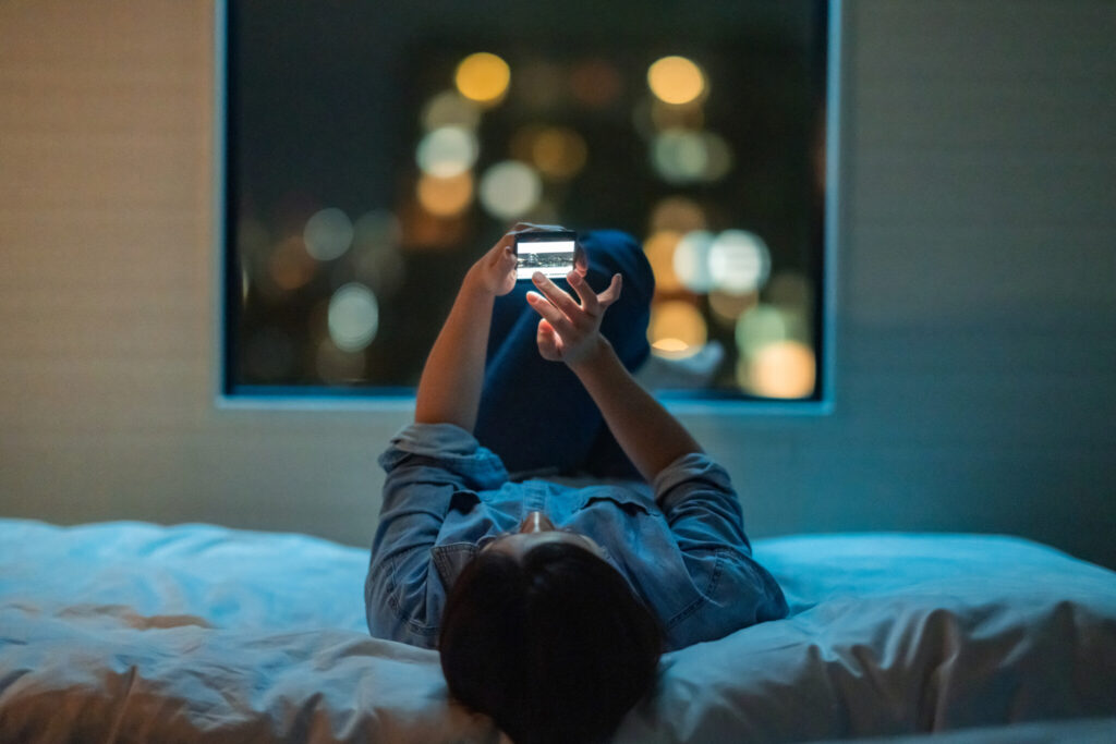 Woman lying down on bed and using smart phone at night