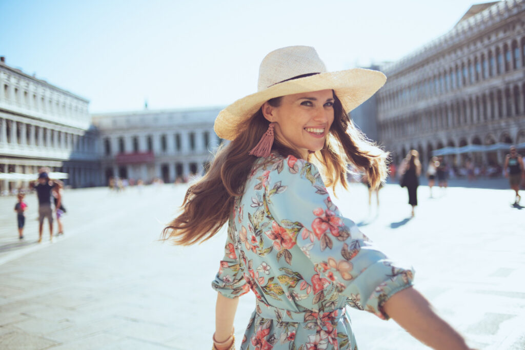 smiling trendy woman in floral dress with hat having excursion
