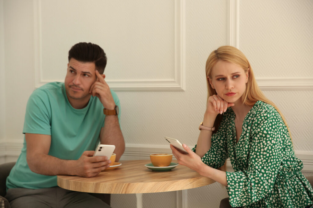 Displeased man and young woman with smartphones in cafe. Failed first date