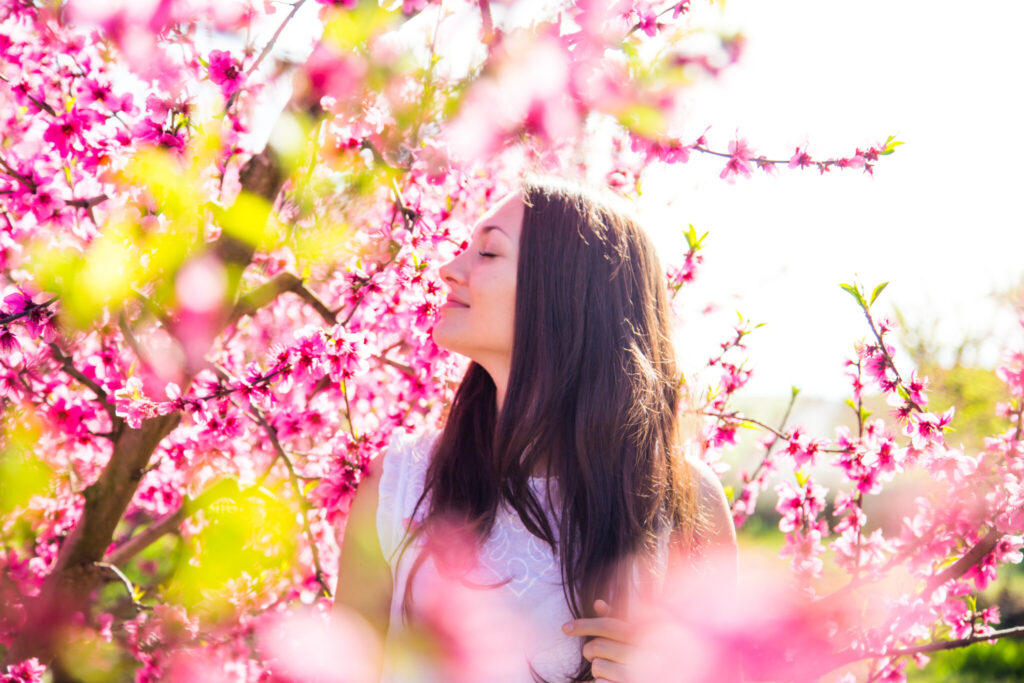 Beautiful russian girl posing between the nice blooming peach trees with pink colors during springtime in a warm day with sunny weather enjoying in the Catalonia countryside.