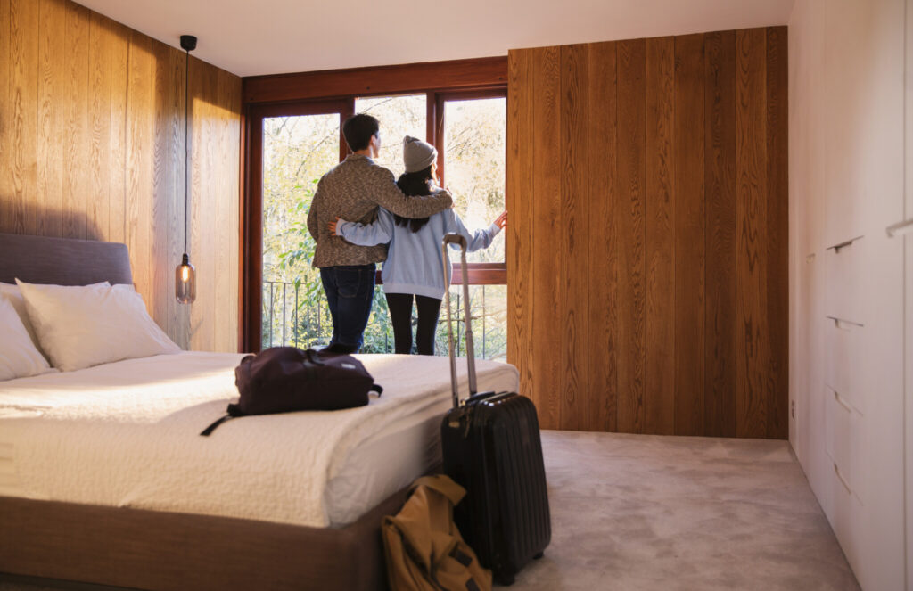 Couple with suitcase looking out bedroom window