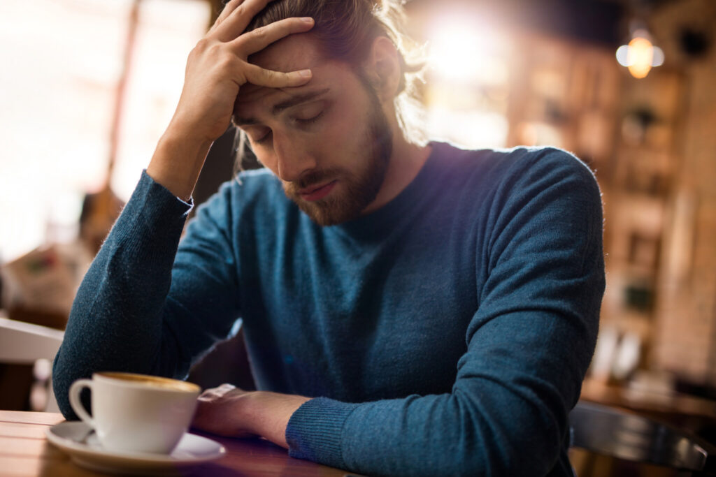 Stressed man holding his head in pain in a cafe.