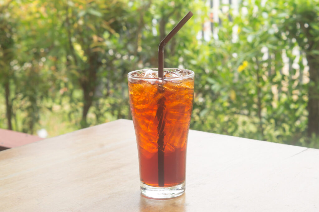 Iced lemon tea with straw in transparent glass on table served at coffee shop or coffee house surrounded by natural condition
