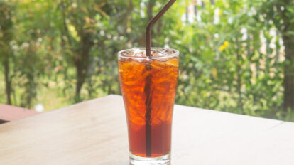 Iced lemon tea with straw in transparent glass on table is served at coffee shop or coffee house surrounded by natural condition.