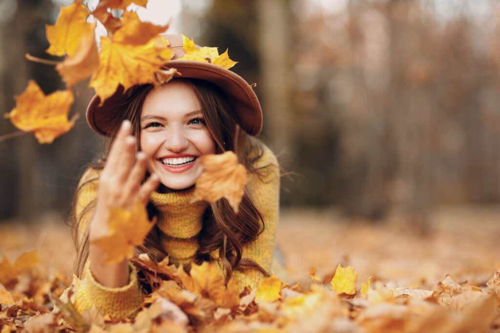 Young woman model in autumn park with yellow foliage maple leaves. Fall season fashion.