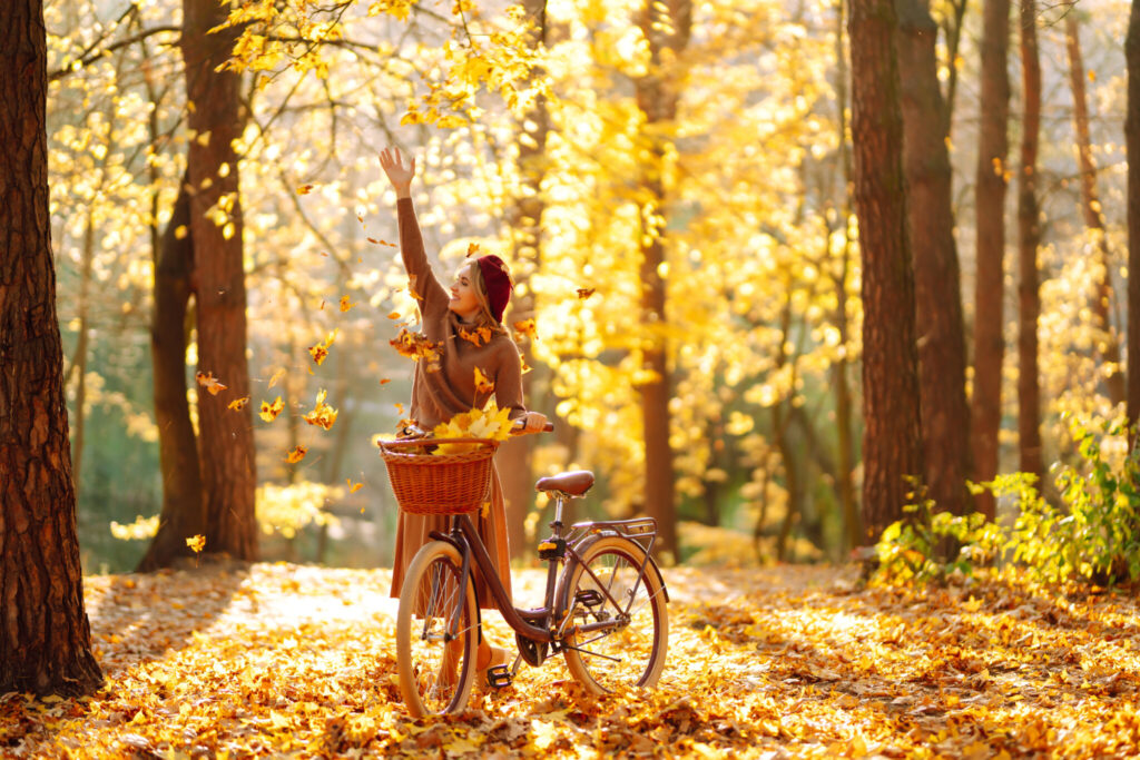 Stylish woman with a bicycle enjoying autumn weather in the park