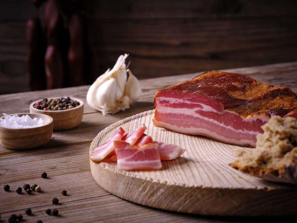 Bacon on wooden board with salt and pepper in bowls, garlic and piece of bread